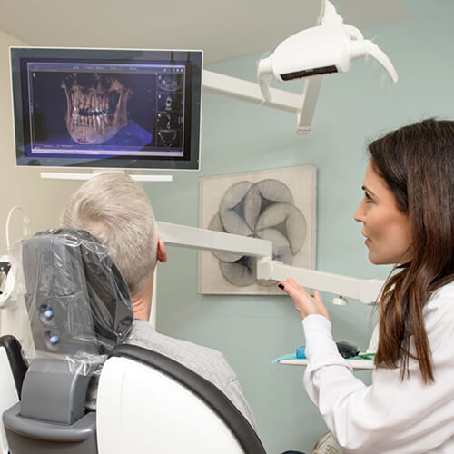 Dr. Becerra, a dentist in Hingham, MA discusses x-rays with a patient in a treatment room 